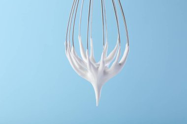 Açık mavi arka planda çırpılmış kremalı çırpma, yakın plan.