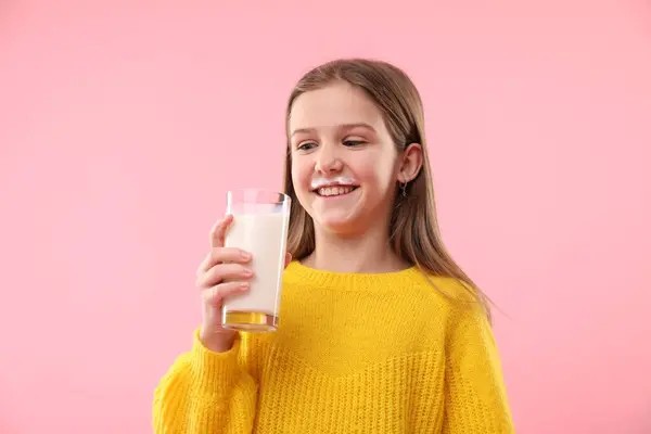 ピンクの背景でおいしい乳製品の飲み物のグラスを保持するミルク口ひげを持つ幸せな少女 — ストック写真