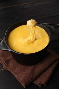 Bir parça jambonu fondü kabına batırıp erimiş peyniri siyah ahşap masaya koymak.