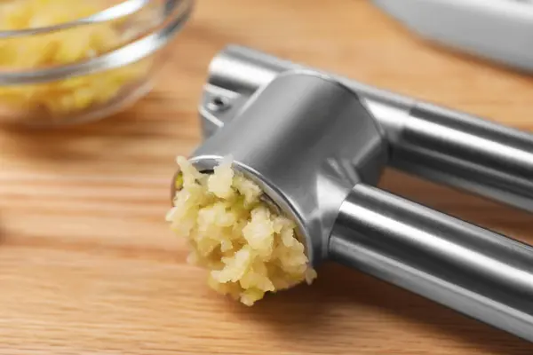 One metal press with crushed garlic on wooden table, closeup