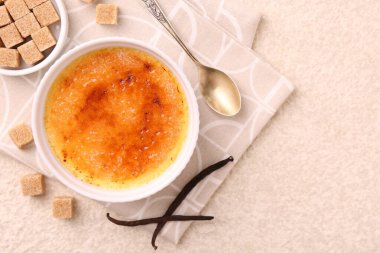 Lezzetli creme brulee kasesi, vanilya kabukları, şeker küpleri ve kaşık desenli masa, üst manzara. Metin için boşluk