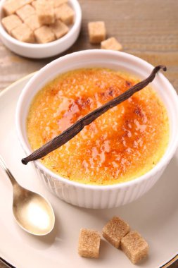Lezzetli creme brulee kasesi, vanilya kapsülü, kaşık ve şeker küpleri masada, yakın plan