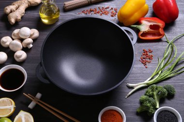 Boş demir tava ve çubuklar koyu gri ahşap masadaki malzemelerle çevrili.