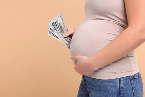 Surrogate mother. Pregnant woman with dollar banknotes on beige background, closeup. Space for text