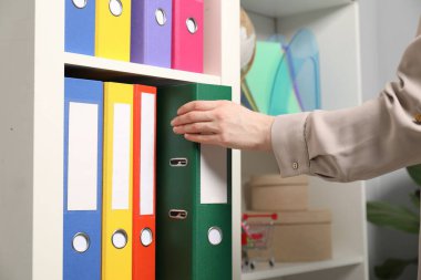 İçerideki raflardan klasör ofis klasörünü alan kadın.