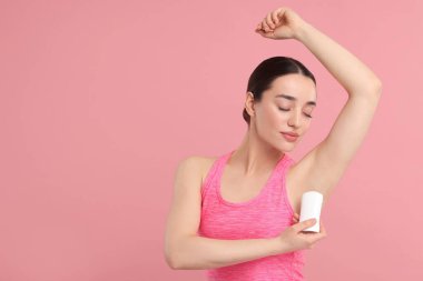 Güzel bir kadın pembe arka plana deodorant sürüyor, metin için boşluk