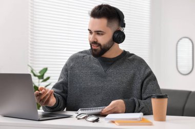 E-öğrenme. Beyaz masa içinde online ders sırasında dizüstü bilgisayar kullanan genç bir adam.