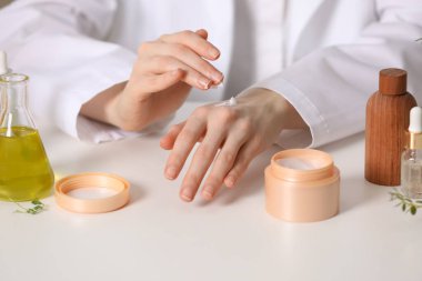 Dermatolog beyaz masada el kremi sürüyor, yakın plan. Kozmetik ürünü test ediliyor