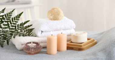 Spa kompozisyonu. Yumuşak gri yüzeyde yanan mumlar, sabunlar, havlular ve lifler.