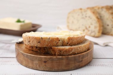 Beyaz ahşap masada tereyağlı lezzetli ekmek dilimleri, yakın plan.