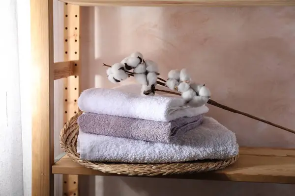 Stacked soft towels and cotton branch on wooden shelf indoors
