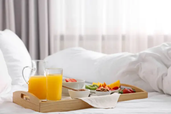 Wooden tray with tasty breakfast on bed at home