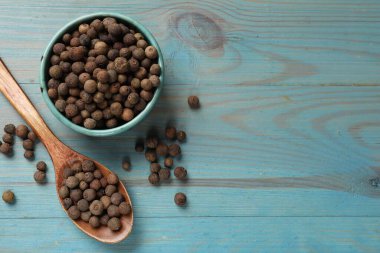 Aromatik biber taneleri kasede ve kaşıklar açık mavi ahşap masada, düz yerde. Metin için boşluk