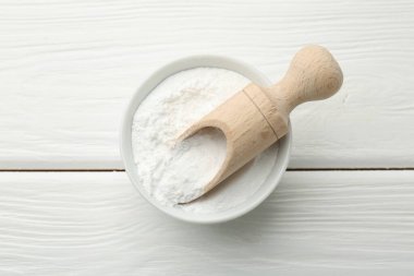 Kabın içinde kabartma tozu ve beyaz ahşap masa üzerinde kepçe, üst görünüm