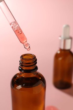 Pipetten şişeye damlatan nemlendirici serum pembe arka planda, yakın plan.