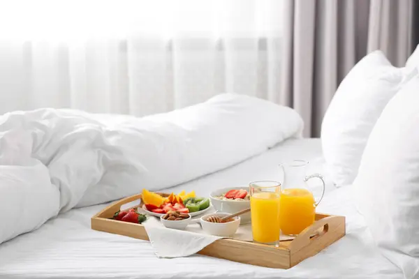 Wooden tray with tasty breakfast on bed at home
