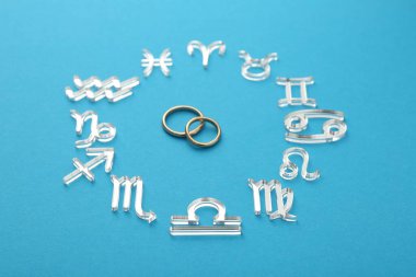 Zodiac signs and wedding rings on light blue background, closeup clipart