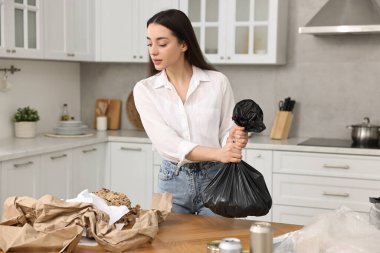 Çöp ayıklama. Mutfaktaki masada plastik çantalı kadın.