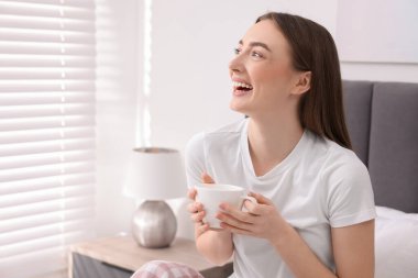 Elinde fincanla güzel bir kadın yatak odasında gülüyor. Metin için boşluk