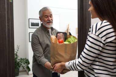 Kurye, içerideki ihtiyara yiyecek dolu kese kağıdı veriyor.