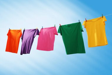 Mavi gökyüzüne karşı çamaşır ipinde kuruyan renkli tişörtler.