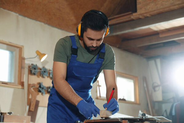 Professional carpenter making mark on wooden bar in workshop