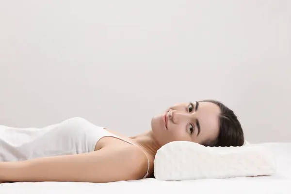 Woman lying on orthopedic pillow against light grey background, space for text