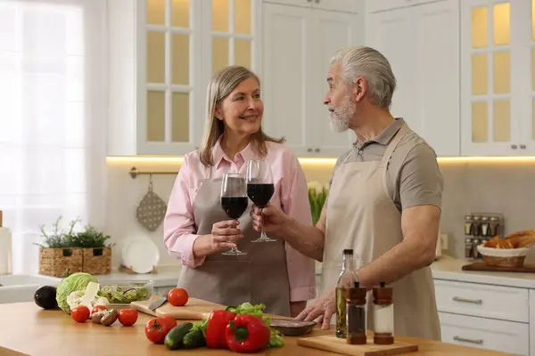 Happy senior couple with glasses of wine cooking together in kitchen