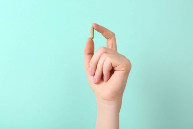 Turkuaz arka planda vitamin kapsülü tutan kadın, yakın plan.