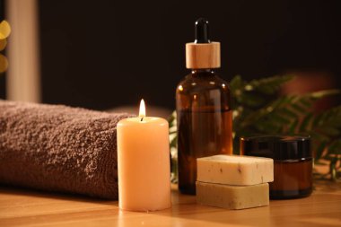 Spa kompozisyonu. Kozmetik ürünler, yanan mum ve havlu ahşap masada.