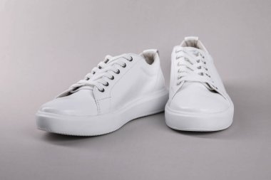 Gri arka planda bir çift şık beyaz spor ayakkabı.