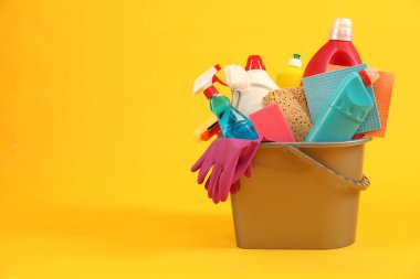Sarı arkaplanda kovadaki farklı temizlik ürünleri, metin için yer