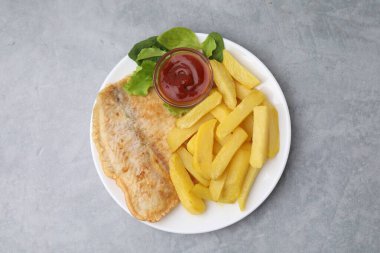 Lezzetli balık ve patates kızartması ketçaplı, ıspanak ve marul gri masada, üst tarafta.