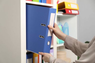 İçerideki raflardan klasör ofis klasörünü alan kadın.
