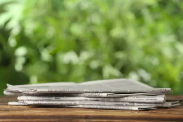 Newspapers on wooden table against blurred green background, space for text. Journalist\'s work