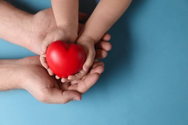 Baba ve çocuğu açık mavi arka planda kırmızı dekoratif kalp taşıyorlar. Metin için boşluk