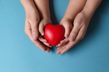 Anne ve çocuğu kırmızı dekoratif kalbi açık mavi arka planda tutuyorlar.