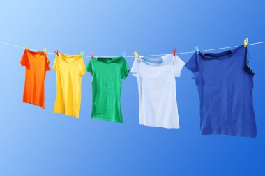 Mavi gökyüzüne karşı çamaşır ipinde kuruyan renkli tişörtler.