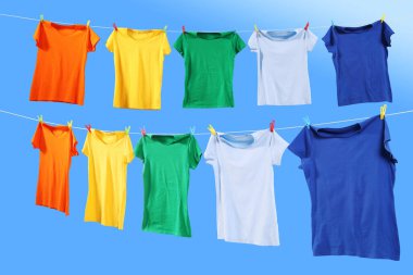 Mavi gökyüzüne karşı çamaşır ipinde kuruyan renkli tişörtler.