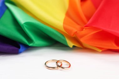 Gökkuşağı LGBT bayrağı ve alyanslar beyaz ahşap masada, yakın plan
