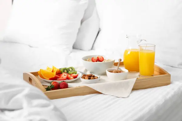 Wooden tray with tasty breakfast on bed