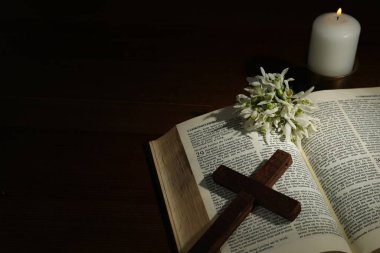 Church candle, Bible, cross and flowers on wooden table, space for text clipart