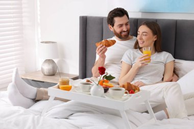 Mutlu çift evde yatakta lezzetli bir kahvaltı yiyor.