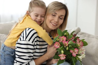 Evde anneler günüyle annesini tebrik eden küçük bir kız. Bir buket alstromerya çiçeği tutan kadın.