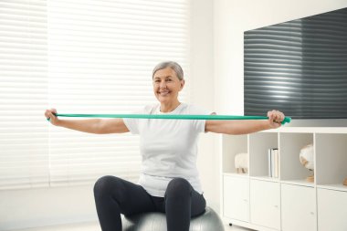 Kıdemli kadın evde spor salonunda elastik direniş bandıyla egzersiz yapıyor.