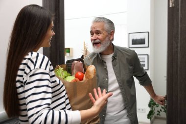 Kurye, içerideki ihtiyara yiyecek dolu kese kağıdı veriyor.