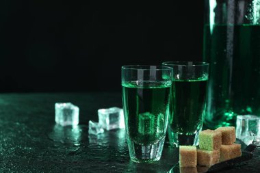 Fondip bardaklarında absent, kaşık, esmer şeker ve buz küpleri gri masada koyu arka planda, mesaj için yer var. Alkolik içki.