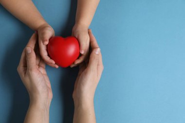 Anne ve çocuğu açık mavi arka planda kırmızı dekoratif kalp taşıyor. Metin için boşluk