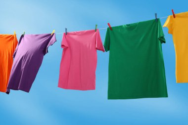 Mavi gökyüzüne karşı çamaşır ipinde kuruyan renkli tişörtler.