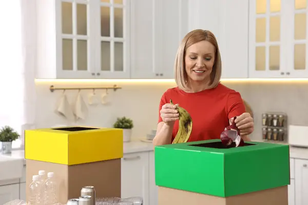 Garbage sorting. Smiling woman throwing food waste into cardboard box in kitchen